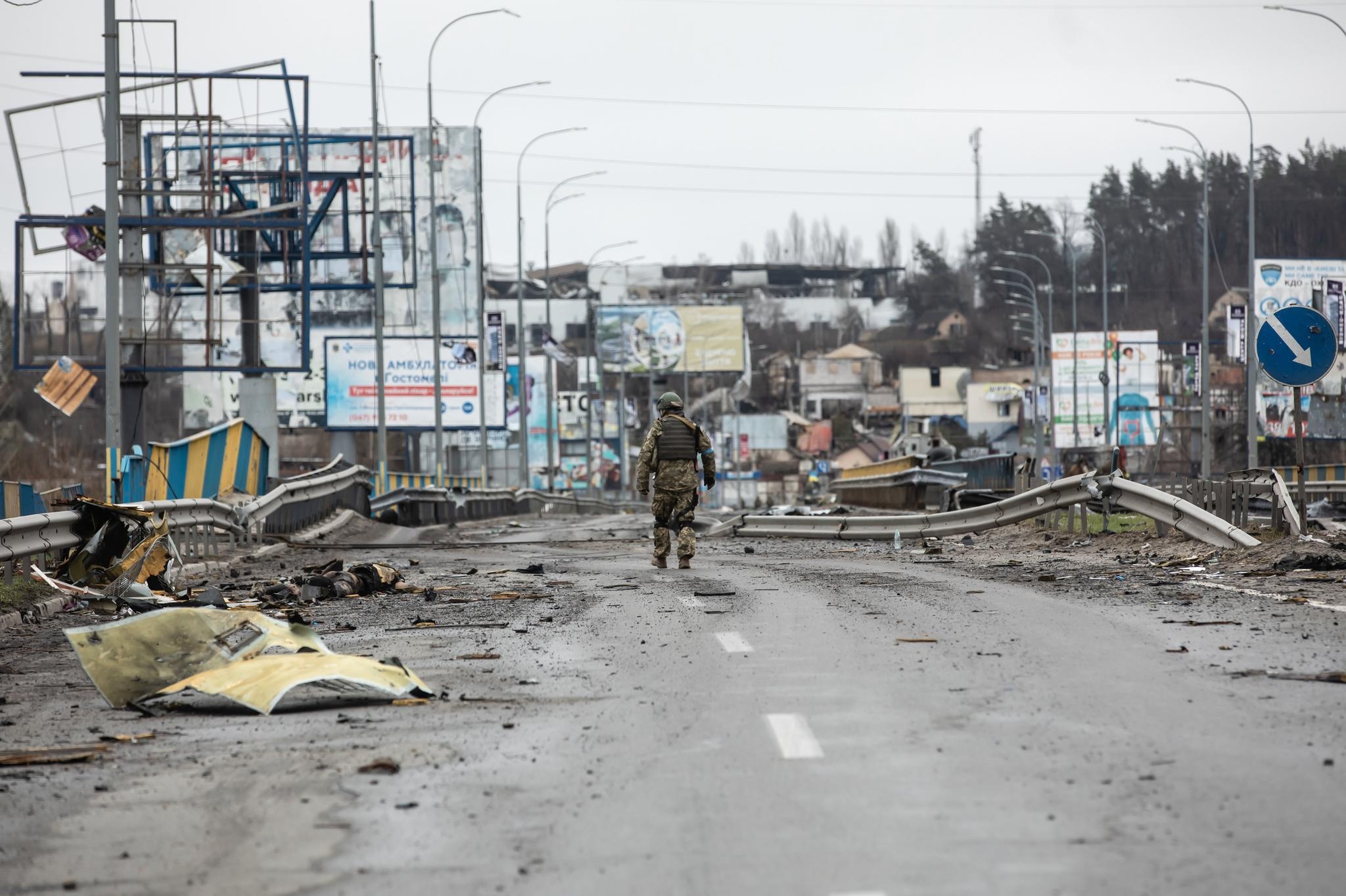 Sotilas kävelee kuolleiden ihmisten ohi Butshassa Ukrainassa huhtikuussa 2022.
