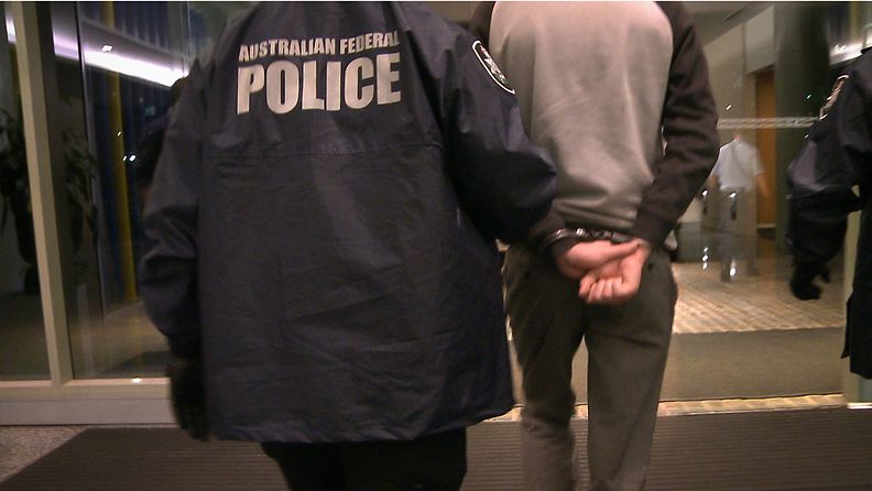 Poliisi taluttaa pidätettyä Australiassa. Kuvituskuva.