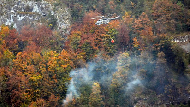 Helikopteri toi sammutusvettä hornetin maahansyöksypaikalle Alpnachstadissa Sveitsissä 23. lokakuuta 2013. 