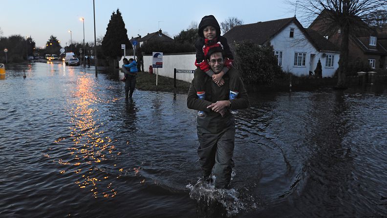 Paikallinen asukas kantaa lastaan tulvien vaivaamassa Surreyssa Britanniassa 13.2.2014.