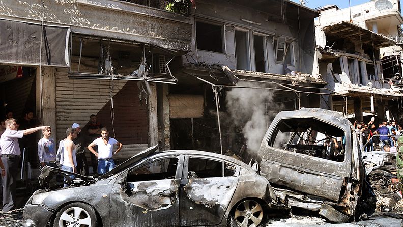 Kaupunkilaiset tutkivat palaneita autoja räjähdyspaikalla Jaramanan asuinalueella Damaskoksessa 25.7.2013.