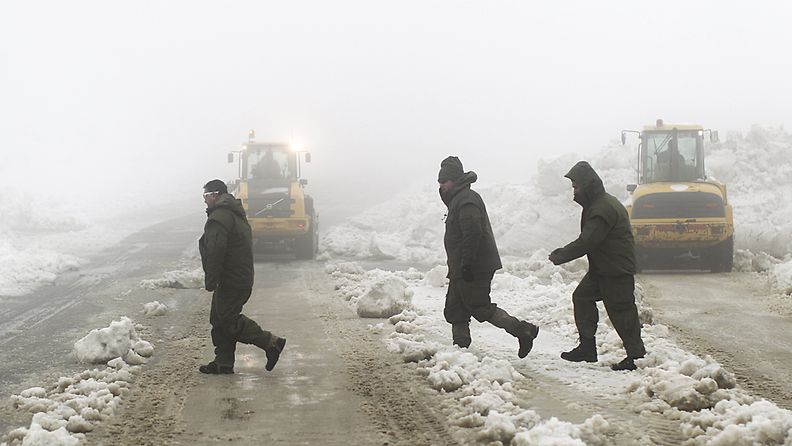 Miehet ylittävät tietä Golanin kukkulalla. Israelin armeijan ajoneuvot auraavat lunta.