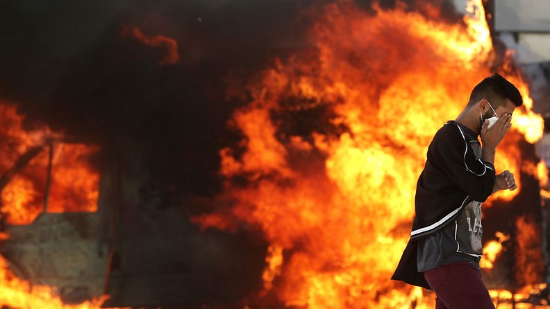  A protester covers his face as he passes in front of a burning vehicle during clashes near Taksim Square in Istanbul, Turkey, 11 June 2013.