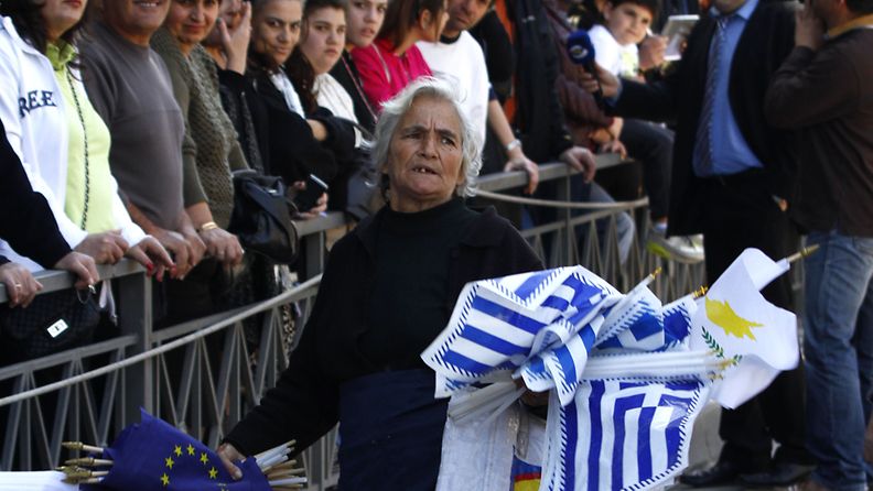 An elderly woman sells flags from Cyprus, Greece and European Union flags during the parade of high school students in front of the Greek Embassy marking the Greek Independence Day in Nicosia, Cyprus, 25 March 2013. Reports state that Cyprus, on 25 March 2013, hammered out a new bailout deal with its international creditors, casting aside a despised bank depositor tax in favour of forced losses on large players in its two biggest lenders. 