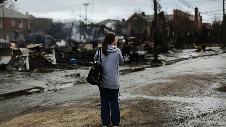 Nainen seisoo Sandyn aikana tulipalossa tuhoutuneiden asuintalojen edessä Queensissä. 