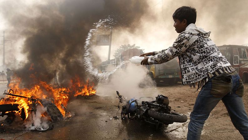 Mies yrittää sammuttaa tuleen sytytettyjä moottoripyöriä Kachpurissa 9.12.2012. 