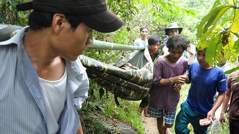 Kuvassa purppuranpunaisessa t-paidassa 41-vuotias Ho Van Lang. 82-vuotiasta isää kuljetetaan pois viidakosta kantoliinassa.
