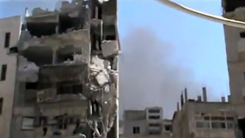 Kuvakaappaus Shaam News Networkin toimittamasta videosta. 16. heinäkuuta 2012 kuvattu video näyttää vaurioituneita rakennuksia ja räjähdysten jälkeistä savua Jouret al-Shiahissa Homsin maakunnassa Syyriassa. 