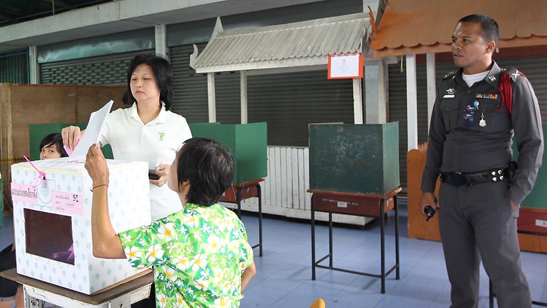 Nainen äänestää Thaimaa parlamenttivaaleissa poliisin tarkkaillessa vaalitapahtumaa Bangkokissa 3.7.2011.