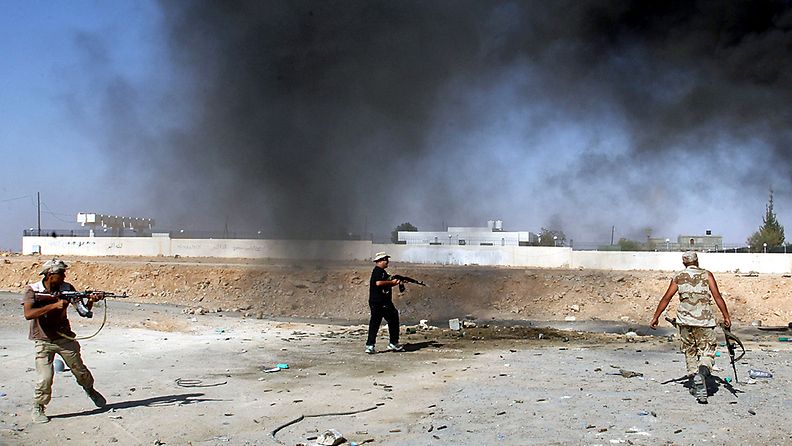 Libyan kapinalliset asemissa Bani Walidissa 18.9.2011. Kuvan ulkopuolella olevasta rakennuksesta nousee mustaa savua. 