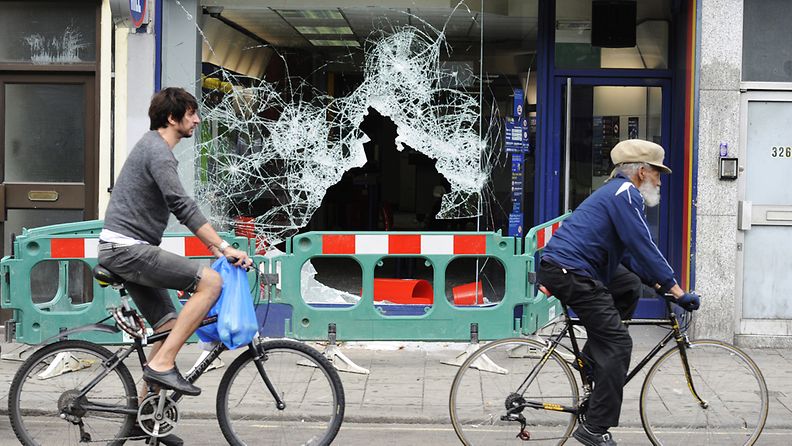 Polkupyöräilijät ohittavat liikkeiden rikottuja ikkunoita Brixtonissa Etelä-Lontoossa 8.8.2011. EPA