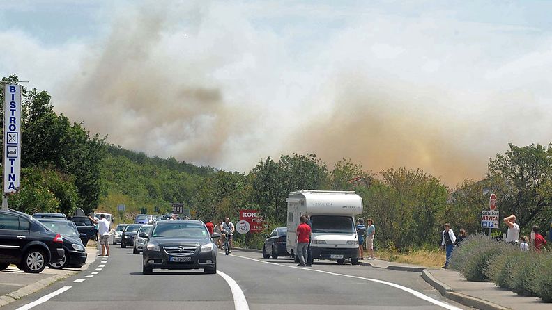 Tourist cars pass along the street as they escape the fire on background near Selce, a small town some 50 km south-east from Rijeka, at the Adriatic coast, 23 July 2012. Croatian authorities have evacuated all tourists from the village and camp because of the fire