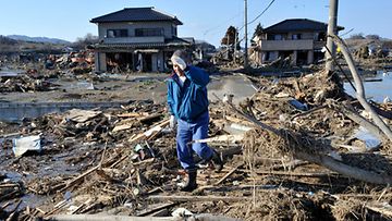 Mies seisoo paikalla, jossa vielä hetkeä aiemmin oli ollut hänen sukulaisensa talo. Se lähti tsunamin mukana. Kuva: EPA