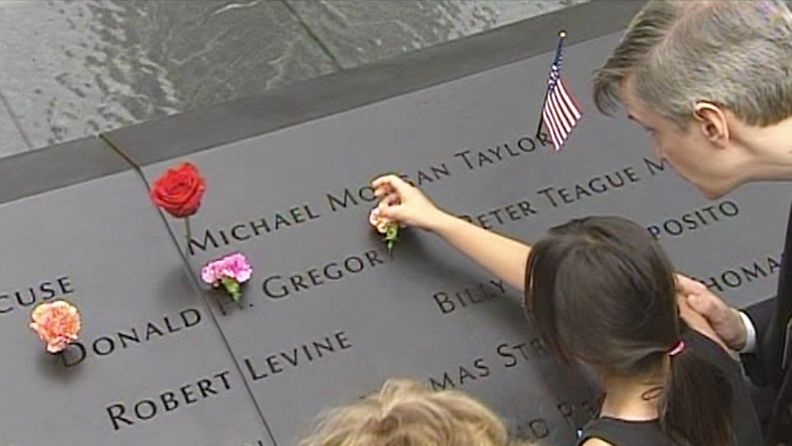 Omaiset asettavat kukkia ja esineitä uhrien nimien kohdalle 9/11-muistomerkillä New Yorkissa.