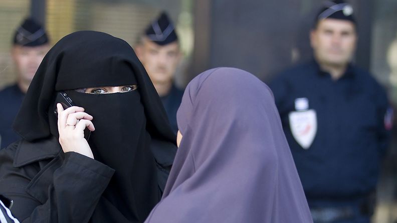 Women wearing niqabs in conversation as police officers stand watch in front of the courthouse in Meaux, near Paris, France, 22 September 2011