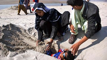 Halvaantunut pikkupoika haudattiin osittain hiekkaan Pakistanissa, jossa säteiden uskotaan parantavan. Kuva: EPA