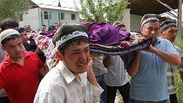 Mies kantaa levottomuuksissa kuolleen naisen ruumista Oshin kaupungissa 15.6.2010. Kuva: Epa