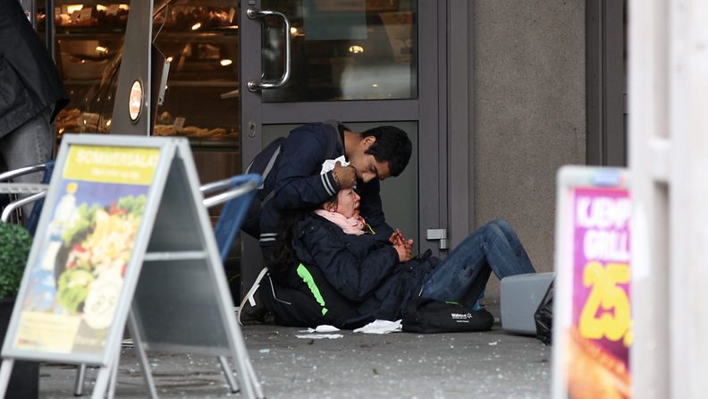 Mies auttaa pommi-iskussa loukkaantunutta naista Oslossa 22.7.2011.