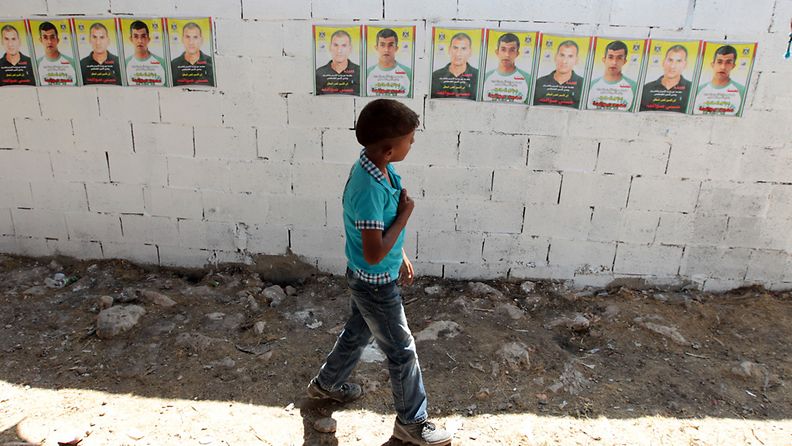 Palestiinalaispoika ohitti muurin, johon oli kiinnitetty Israelin eilen vapauttamien palestiinalaisvankien kuvia. Azmoutin kylässä 14.8.2013.