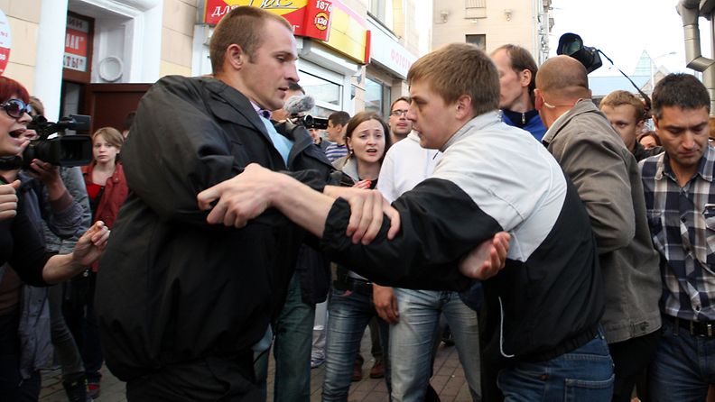 Mustaan takkiin pukeutunut poliisi (vas.) taltuttaa mielenosoittajaa Minskissä 3.7.2011.