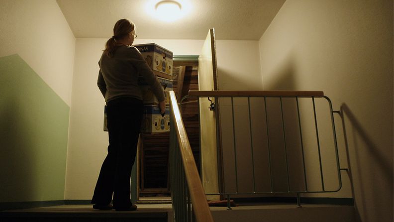 Nainen kantaa pahvilaatikkoja kotiovesta sisään.