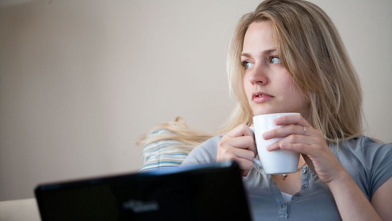 Surullinen nainen juo kahvia tietokoneen äärellä