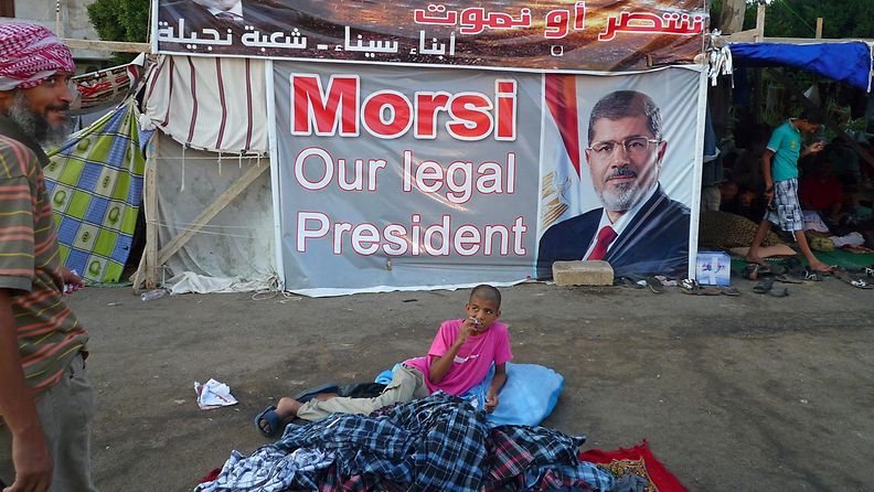 Lapsi leiriytyneenä Mursin kuvan vierelle. Kuva Muslimiveljeskunnan mielenosoituksesta viime syksynä.