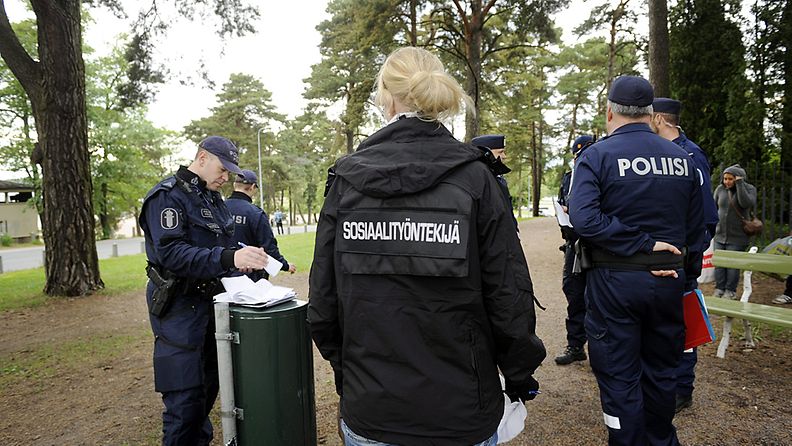 Poliisi kirjoittaa roskiksen päällä rikesakkoa alaikäiselle alkoholijuoman hallussapitäjälle (sosiaalityöntekijän takana) Hietaniemen uimarannan vieressä koulujen päättäjäisjuhlintapäivänä Helsingissä 2. kesäkuuta 2012.