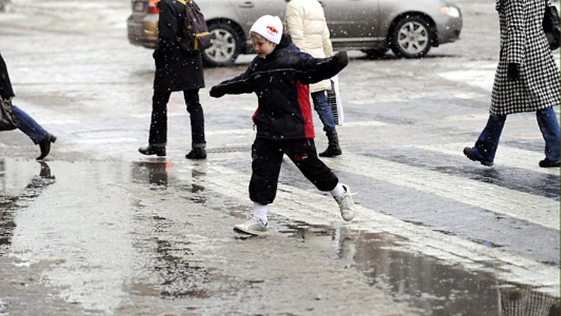 Jalankulkijat hyppivät vesilammikkojen yli Mannerheimintiellä Helsingissä lumien sulaessa pitkän pakkaskauden ja lumisateiden jälkeen 1. maaliskuuta 2010