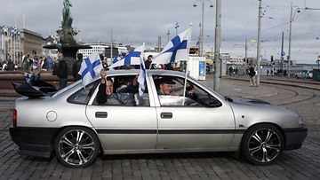 Ihmiset hehiluttavat Suomen lippuja auton ikkunasta ennen Suomen jääkiekkomaajoukkueen kultajuhlien alkua Kauppatorilta Helsingissä 16. toukokuuta 2011. Kuva: Lehtikuva