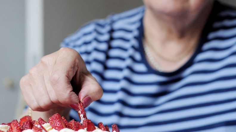 Vanhempi nainen koristelee mansikkakakkua. Kuva: Lehtikuva