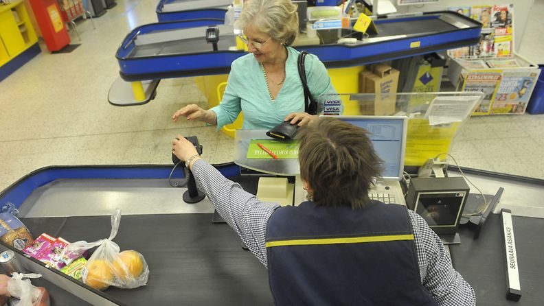  Tallenna  Myyjä opastaa iäkästä naista korttimaksussa supermarketissa.