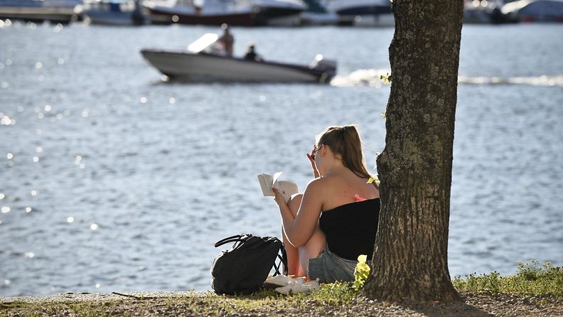 Nainen lukee kirjaa rannassa Helsingissä 3. heinäkuuta 2015.