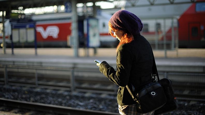 nainen käyttää puhelinta juna-asemalla