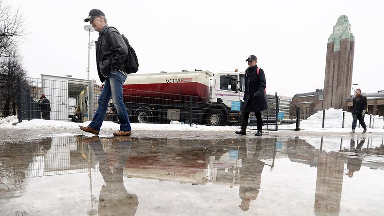 Jalankulkijoita kävelemässä jään ja lätäköiden peittämällä Rautatientorilla Helsingissä 27. tammikuuta 2016.