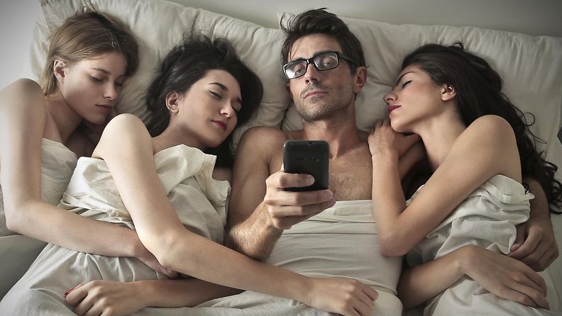 Mies ja kolme naista nukkumassa – mies käyttää älypuhelintaan.
