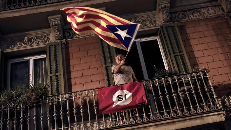 Mies heiluttaa Katalonian lippua parvekkeella levottomuuksien täyttämän itsenäisyysäänestyksen päivän iltana.