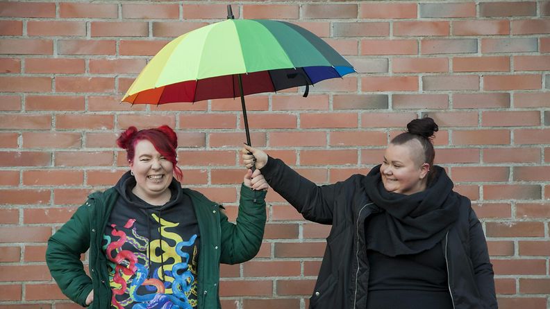 Sateenkaarinuorisotyöntekijät Mari-Katri Lempinen ja Emmi Erkkilä pitelevät sateenkaaren väristä sateenvarjoa.