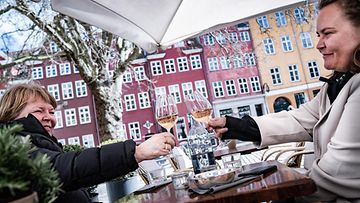 Kaksi hymyilevää asiakasta kilistämässä viinilasejaan terassilla Kööpenhaminassa.