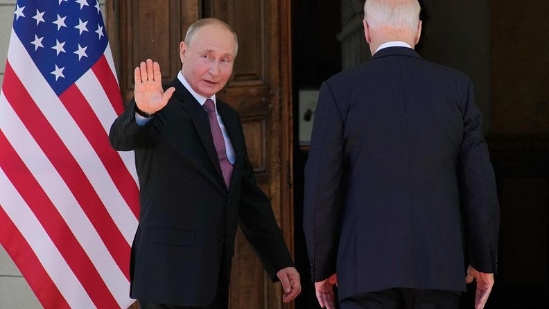 Vladimir Putin vilkuttaa taakseen kun hän astuu Joe Bidenin kanssa ovesta sisään Geneven huippukokouksessa.