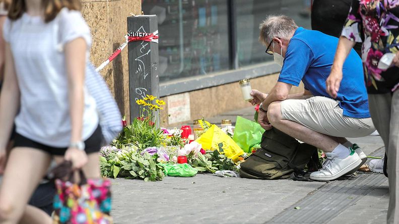 Mies on kyykistynyt kukkakimppujen äärelle, jotka on laskettu kadulle puukotuksen uhrien muistoksi.