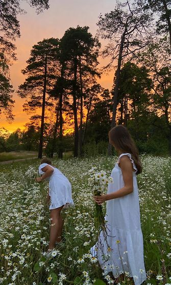 Kaksi naista poimii kukkia niityllä valkoisissa mekoissa.