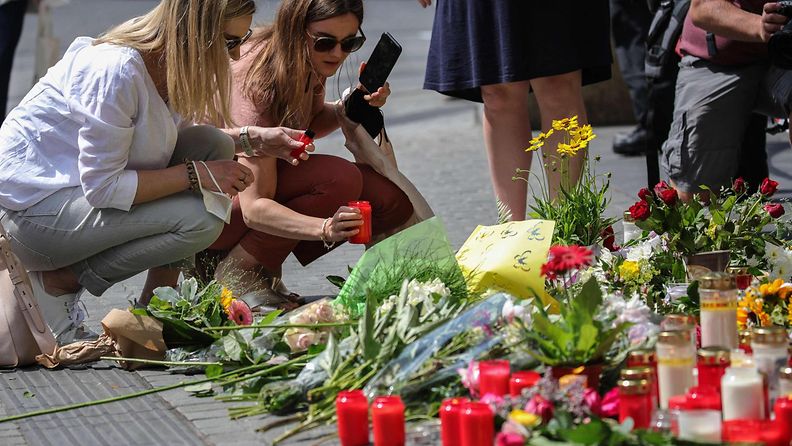 Kaksi naista on kyykistynyt asettamaan kynttilää puukotuksen uhrien muistopaikalle.