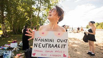 Meri-Maija Näykki pitelee tissiflashmobissa kylttiä, johon on maalattu naisen rinnat ja teksti: "Nännini ovat neutraalit vaikka sinun mielesi olisi likainen"."