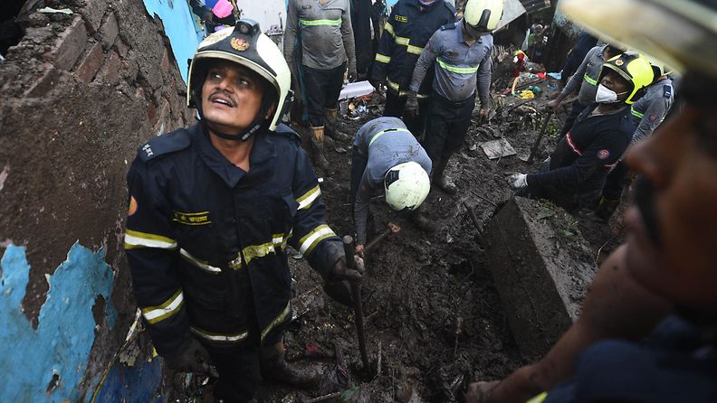 Pelastushenkilöstö tutkii tuhoisan maanvyöryn jälkiä. Kypäräpäinen mies katselee yläviistoon toisen kaivaessa.