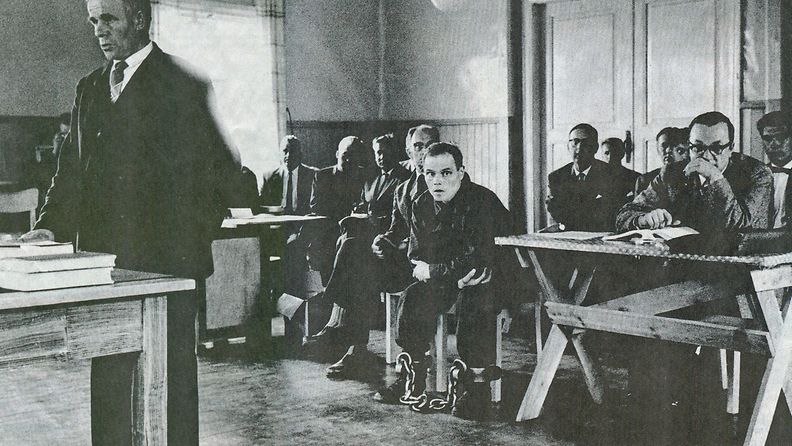 Runar Holmström istuu keskellä huonetta oikeudenkäynnissä. Jalat on kahlittu paksuilla kahleilla.