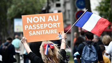Mieltä osoittava nainen pitelee Ranskan lippua ja oranssia kylttiä jossa lukee "Ei terveyspassille". 