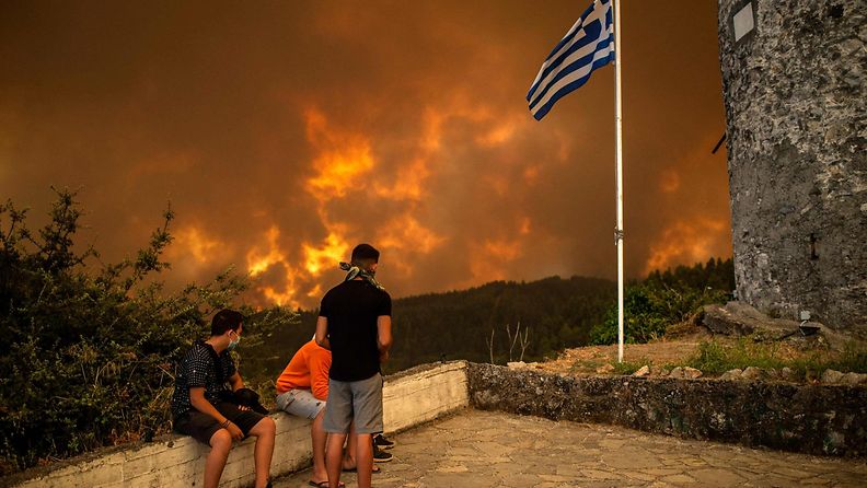 Kundit ihmettelee palon keltaiseksi värjäämää maisemaa Kreikan lipun liehuessa salossa.
