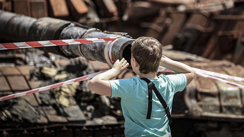 Lapsi tutkii tuhoutunutta panssarivaunua Ukrainassa kesäkuussa 2022.
