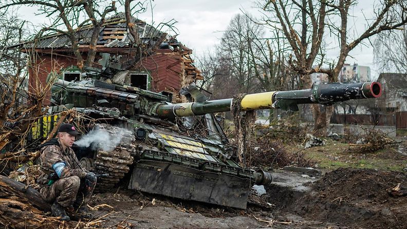 Tuhottu venäläinen tankki ja sotilas tupakalla huhtikuussa 2022.